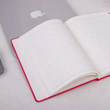 Red Fluct PRO A5 Diary - Work Diary open on desk beside laptop, featuring ruled pages and date headers for goal tracking and daily planning.