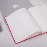 Red Fluct PRO A5 Diary - Work Diary open on desk beside laptop, featuring ruled pages and date headers for goal tracking and daily planning.