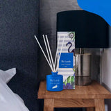 Blue diffuser with packaging on a wooden nightstand next to a black lamp.