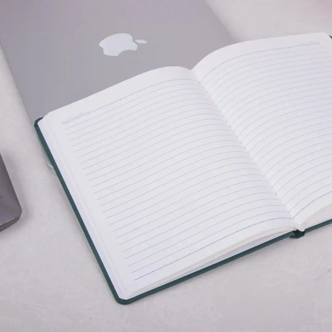 Grey Fluct PRO A5 Diary open on a desk beside a laptop, showcasing lined premium pages for organized planning and daily work journaling.