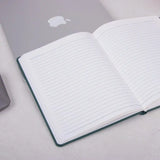 Grey Fluct PRO A5 Diary open on a desk beside a laptop, showcasing lined premium pages for organized planning and daily work journaling.