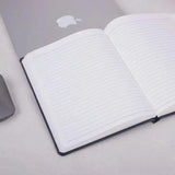 Black Primo A5 Diary with 80GSM lined pages open on a desk beside a laptop. Ideal for productivity planning and daily goal tracking.