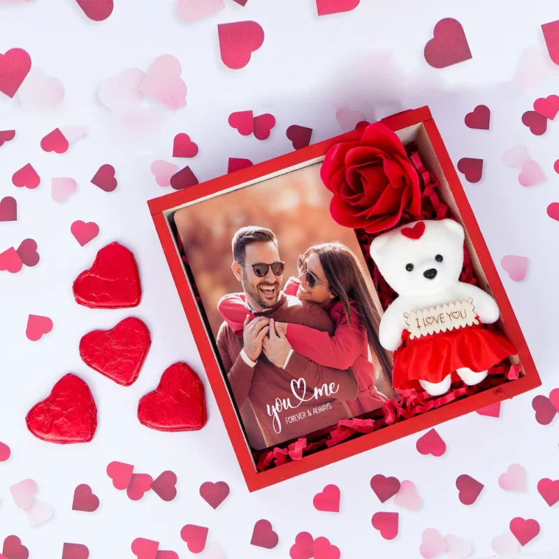 Personalized teddy gift set with photo card, red rose, white teddy, and heart-shaped chocolates in pinewood tray for Valentine's Day.