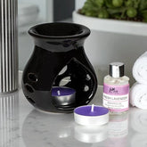 Black ceramic oil burner with a purple candle and a bottle of lavender scented oil on a marble surface.