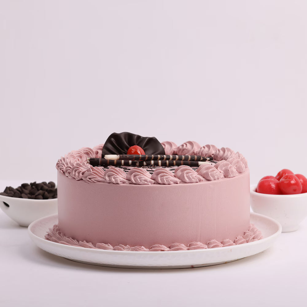 Side view of Chocolate Glory Cake - smooth pink cream cake with chocolate decorations and cherries, great for special occasions.