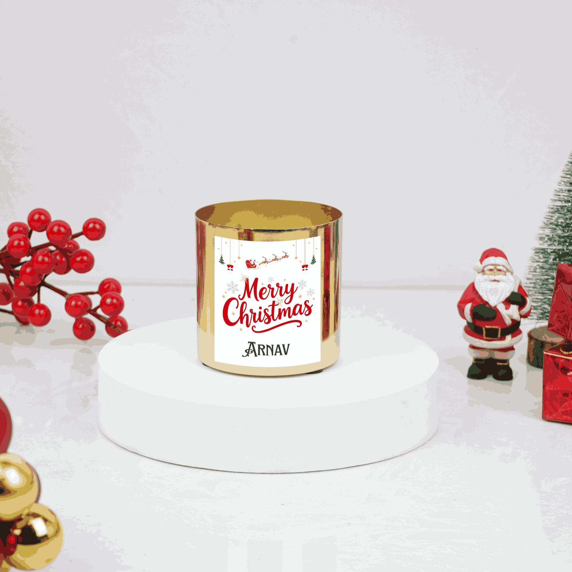 Gold candle with 'Merry Christmas Arnav' text, surrounded by Christmas decorations on a white background