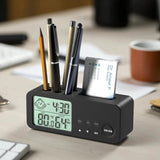 Black digital desk organizer with clock, pen holder, and card slot on a desk.