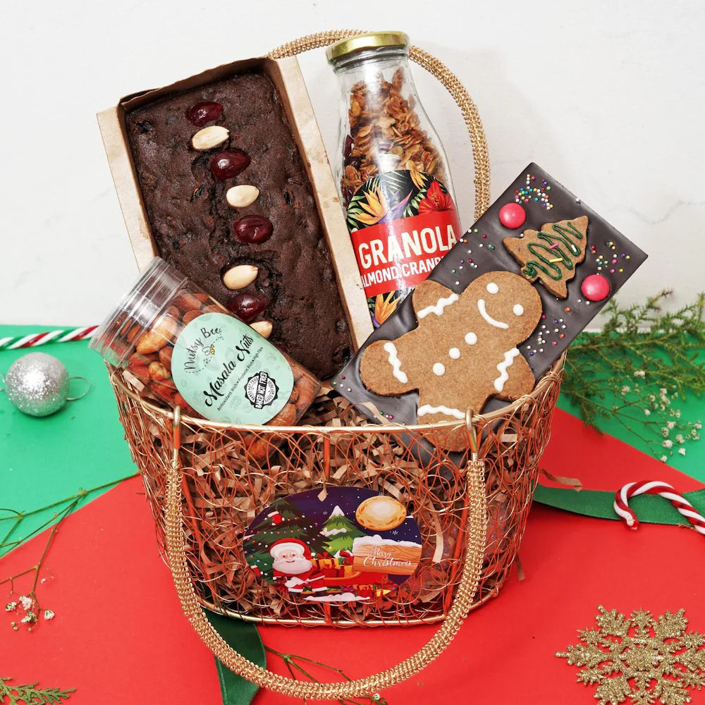 Fusion of Flavors Christmas Hamper with holiday-themed treats including plumcake, granola, masala nuts, and gingerbread chocolate in a festive basket.