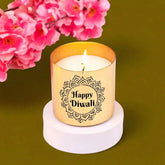 Candle with 'Happy Diwali' design on a white base, surrounded by pink flowers on a green background