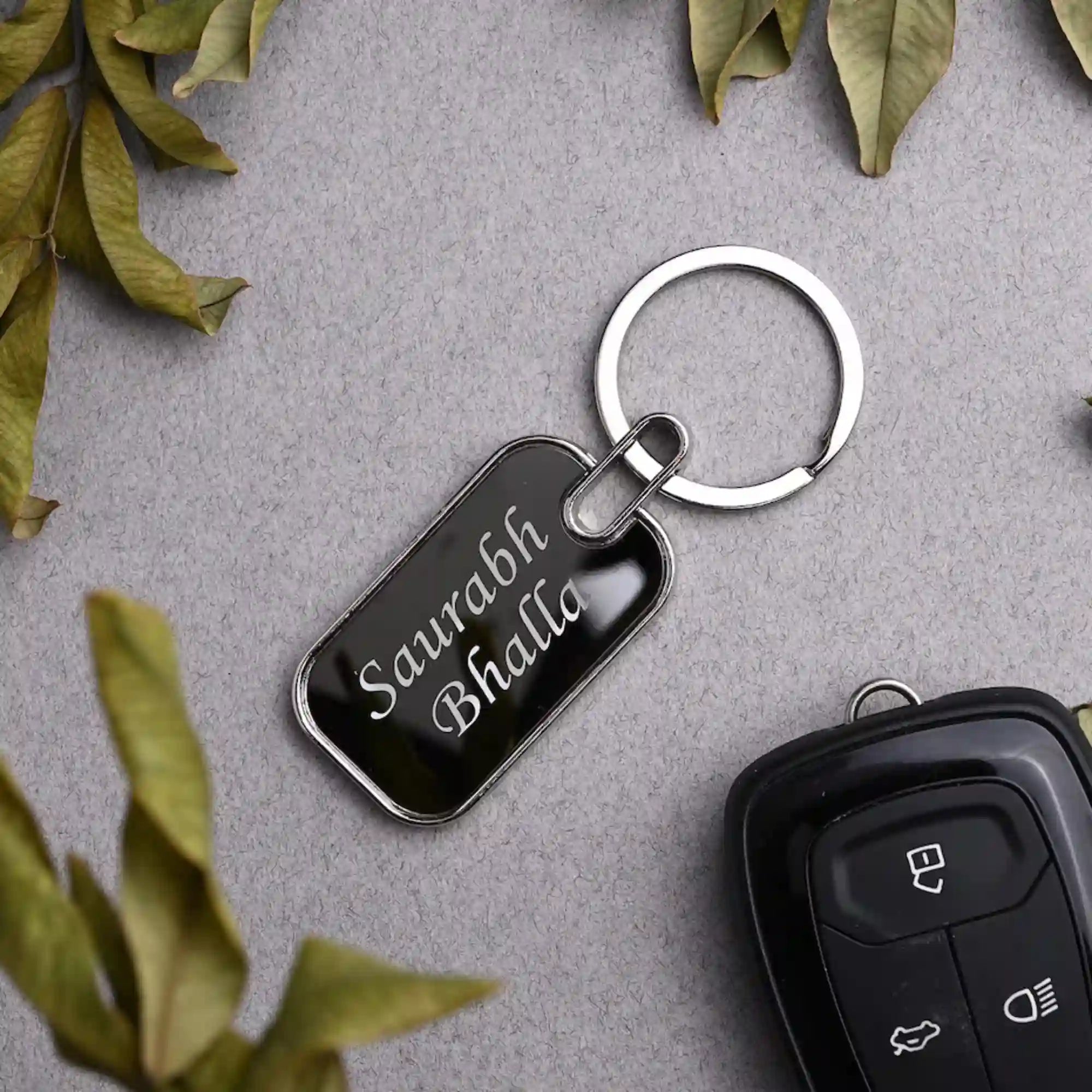Keychain with engraved name on a gray surface with leaves around