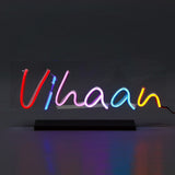 Personalized Name Neon Sign 'Vihaan' in colorful LED lights on a clear acrylic panel with black stand, great for birthdays or festive décor.