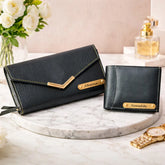 Two black handbags with gold accents on a marble surface, accompanied by flowers and a perfume bottle.