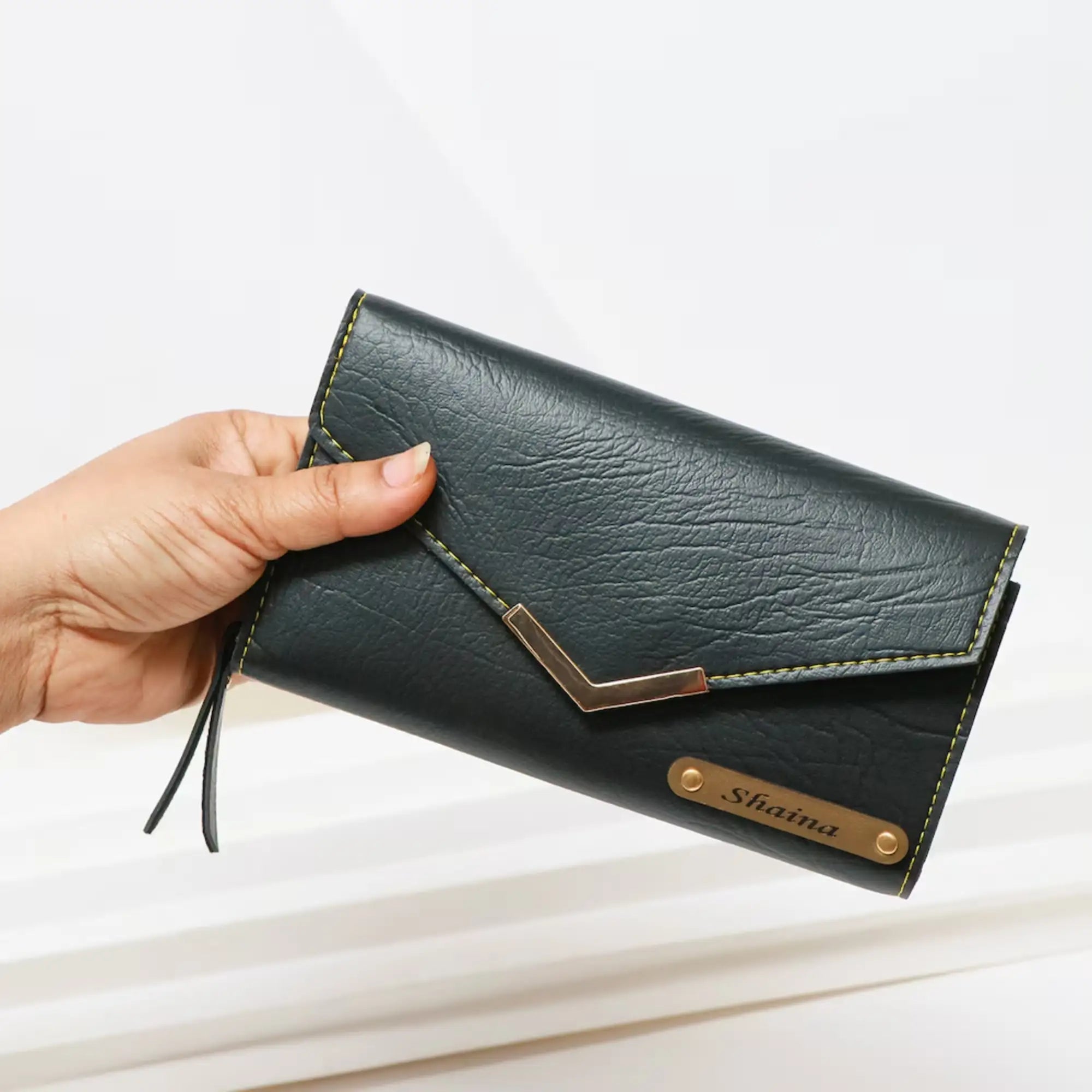 Hand holding a black wallet with gold accents on a light background