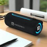 Black Portronics Bluetooth speaker on a wooden desk