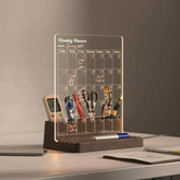 Transparent monthly planner with stationery items on a wooden stand against a neutral background