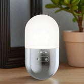 White LED night light with XECH branding on a wooden surface, surrounded by a plant and framed picture.