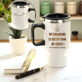 White travel mug with black handle and interior, featuring text, on a marble surface with a plant and notebook.