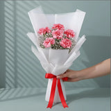 Close-up of pink carnations in bouquet wrapped in white paper with red ribbon