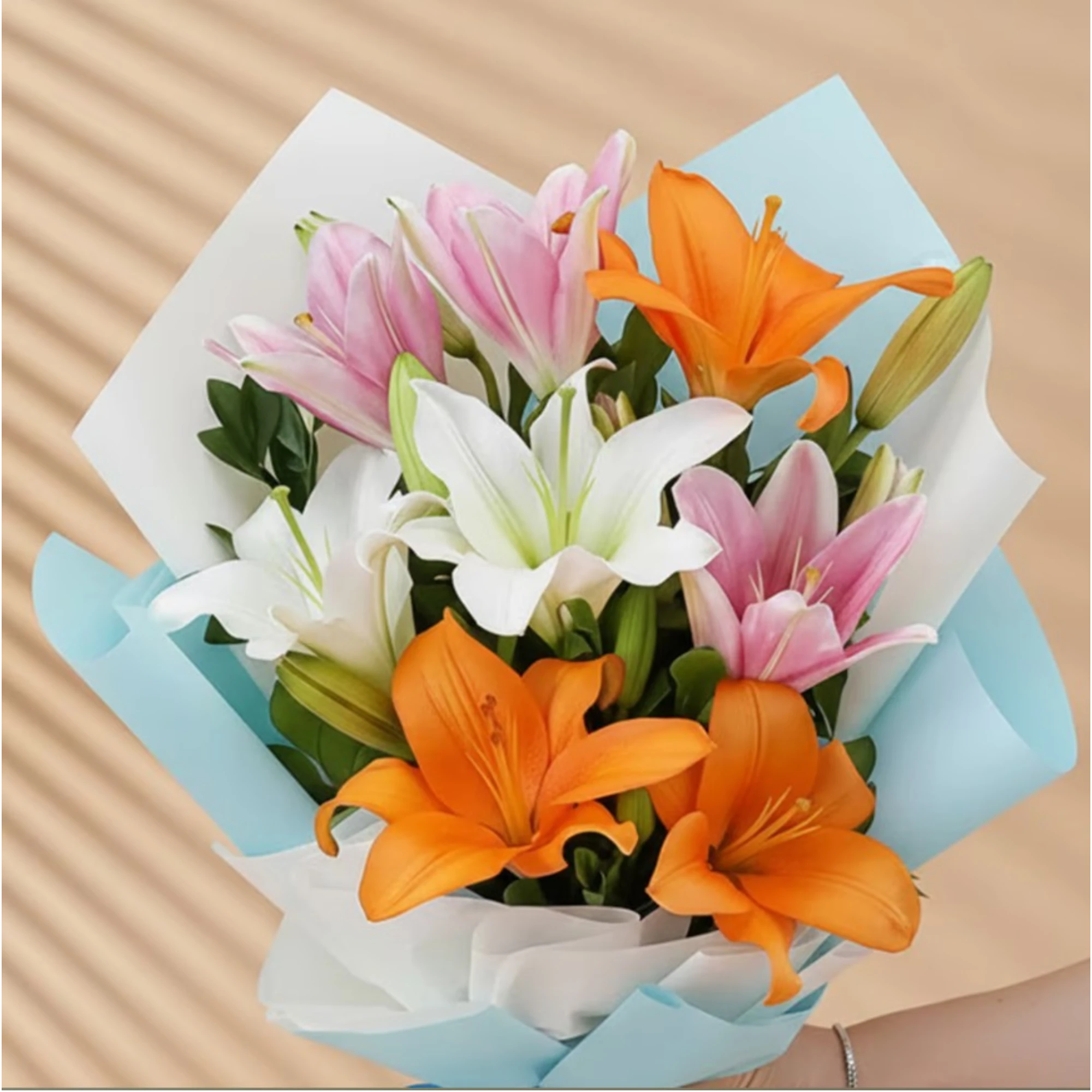 Close-up of mixed Asiatic lilies bouquet with pink, white, and orange blooms wrapped in blue paper