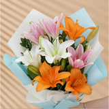 Close-up of mixed Asiatic lilies bouquet with pink, white, and orange blooms wrapped in blue paper