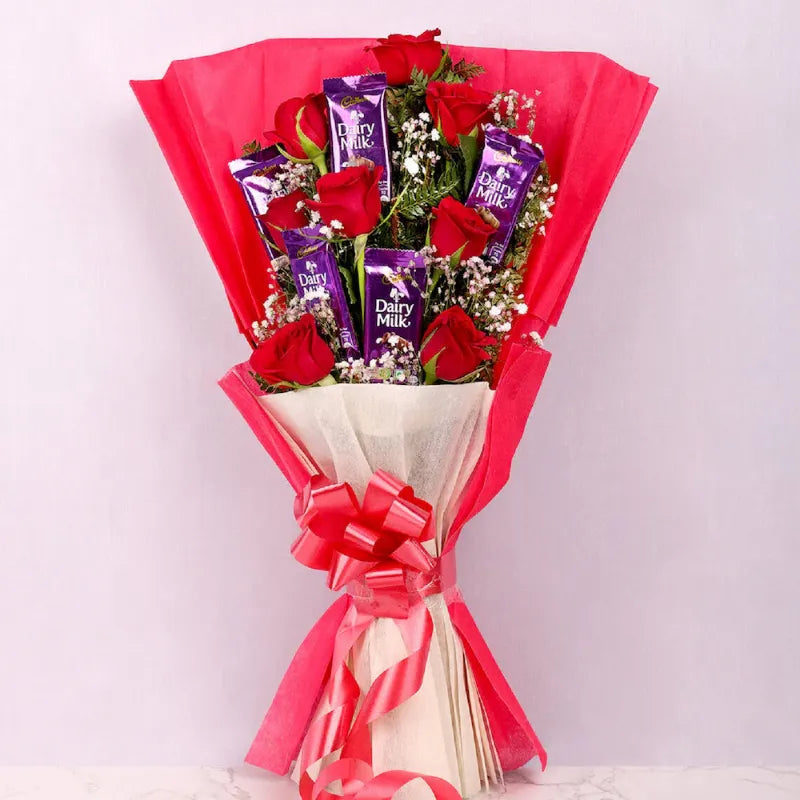 Valentine's Day Roses and Chocolate Gift Arrangement featuring red roses and Dairy Milk chocolates in a pink bouquet wrap with ribbon.