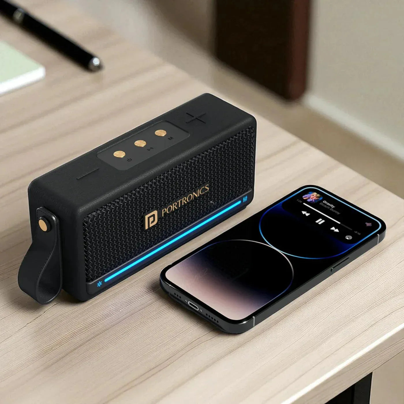 Black portable speaker with Portronics branding next to a smartphone on a wooden surface.