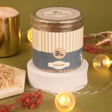 Jar of Bajra Flakes from The Daily Nut Co on a green surface with decorative elements.