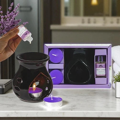Aromatherapy set with black diffuser, purple candles, and a bottle of 'Fresh Lavender' oil on a marble surface.