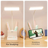 Desk lamp with smartphone holder on a wooden surface, featuring stationery items.