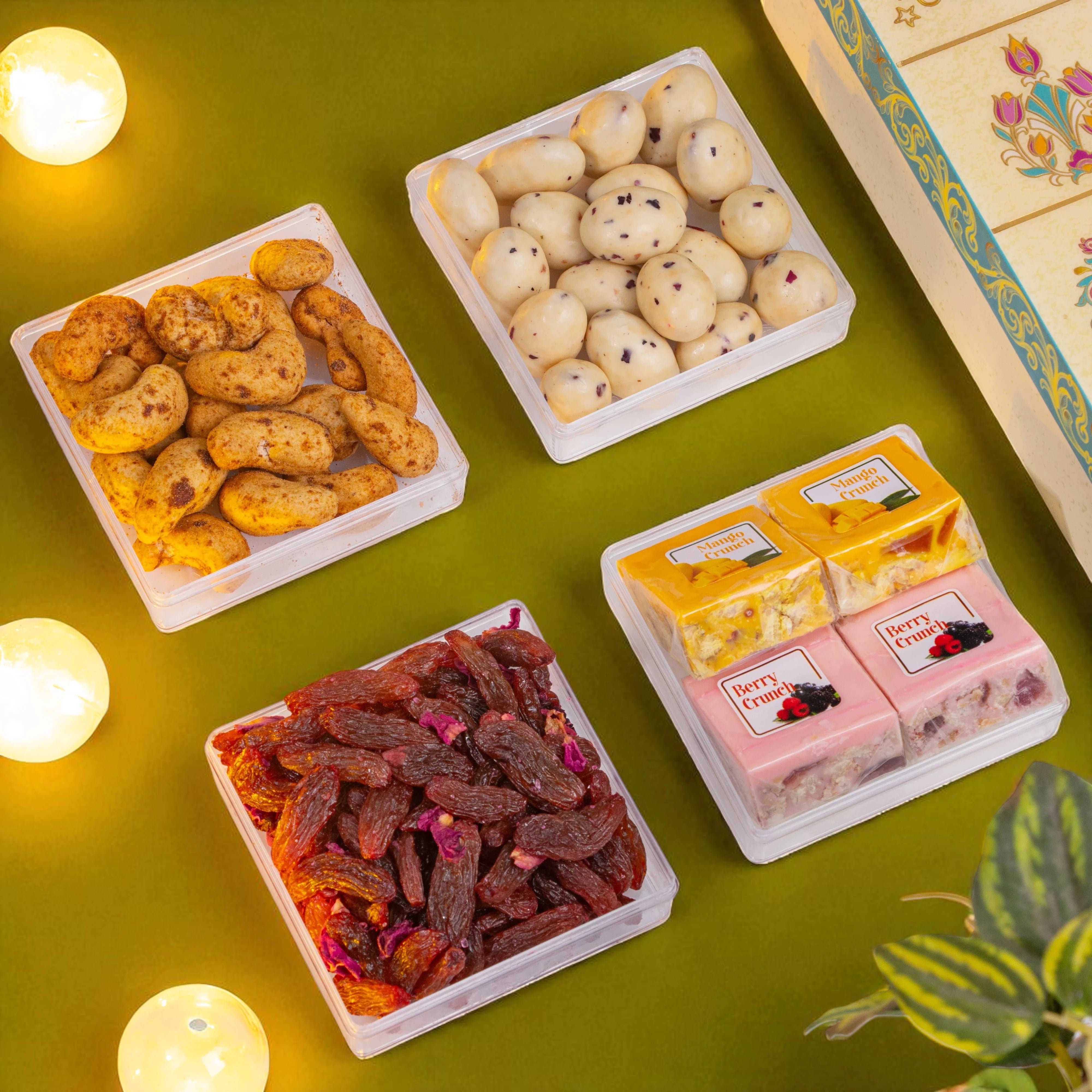 Assorted snacks in small containers on a green surface with decorative elements.