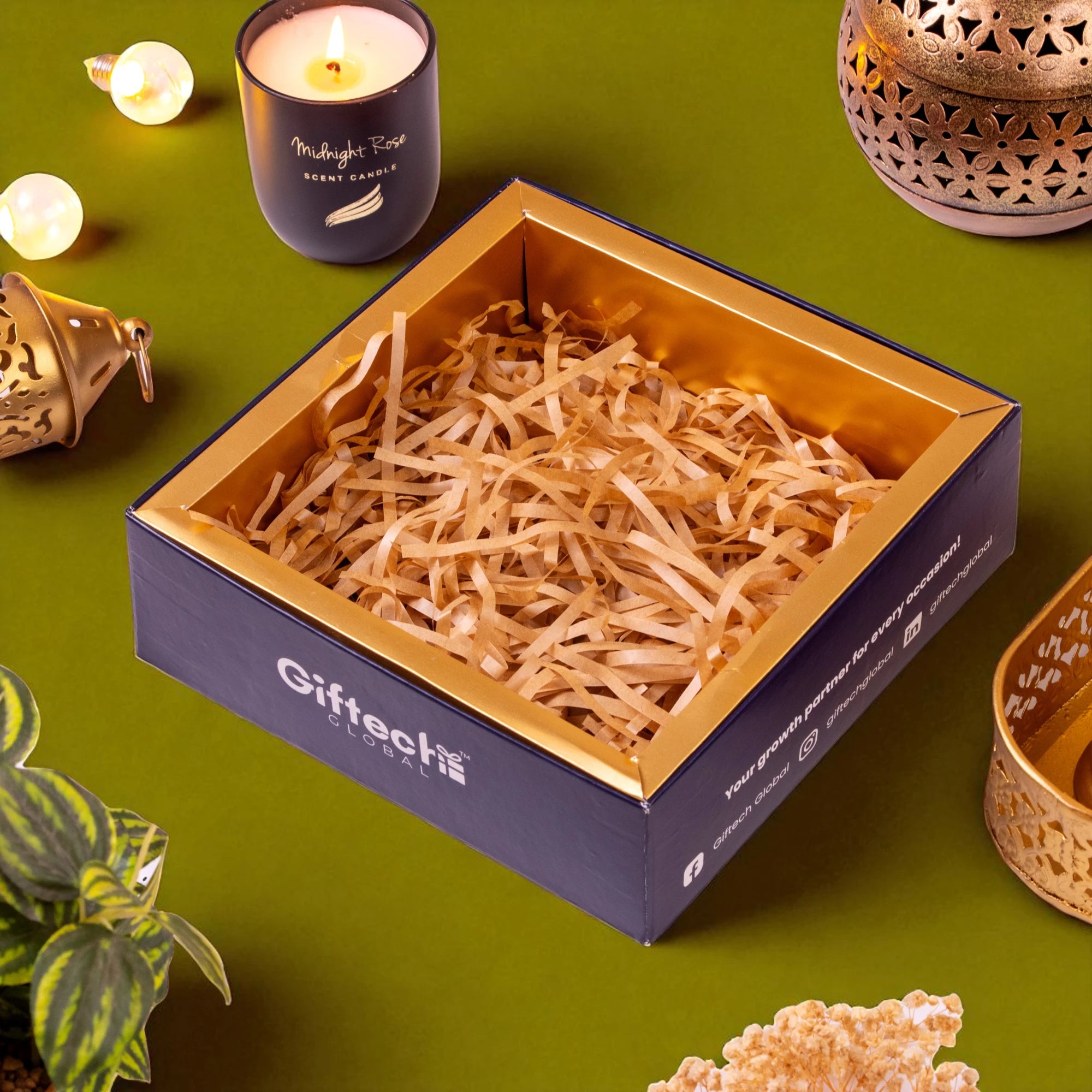 Gift box with shredded paper on a green surface with candles and decorative items.