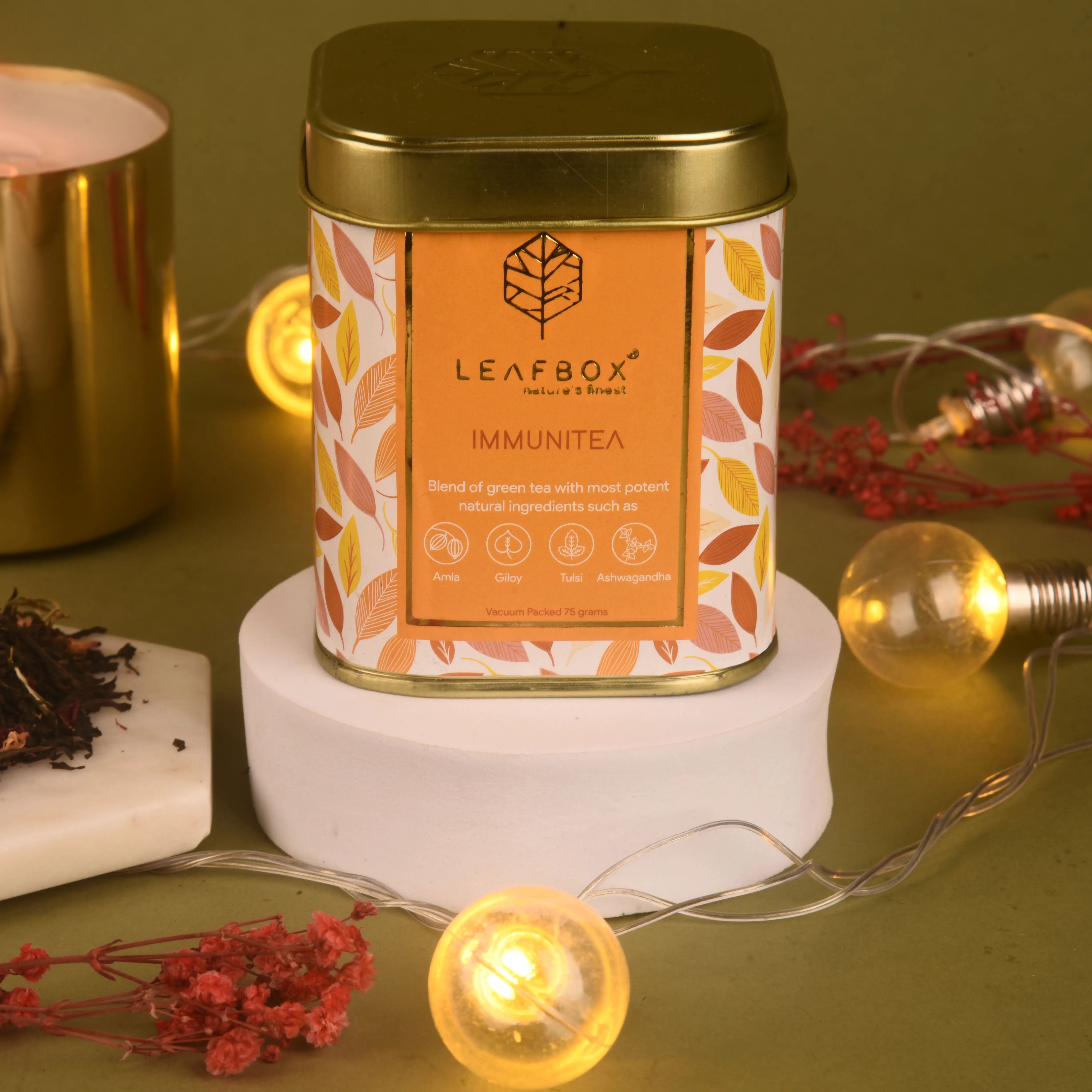 Leafbox Immunitéa tea canister on a decorative stand with warm lighting and red flowers.