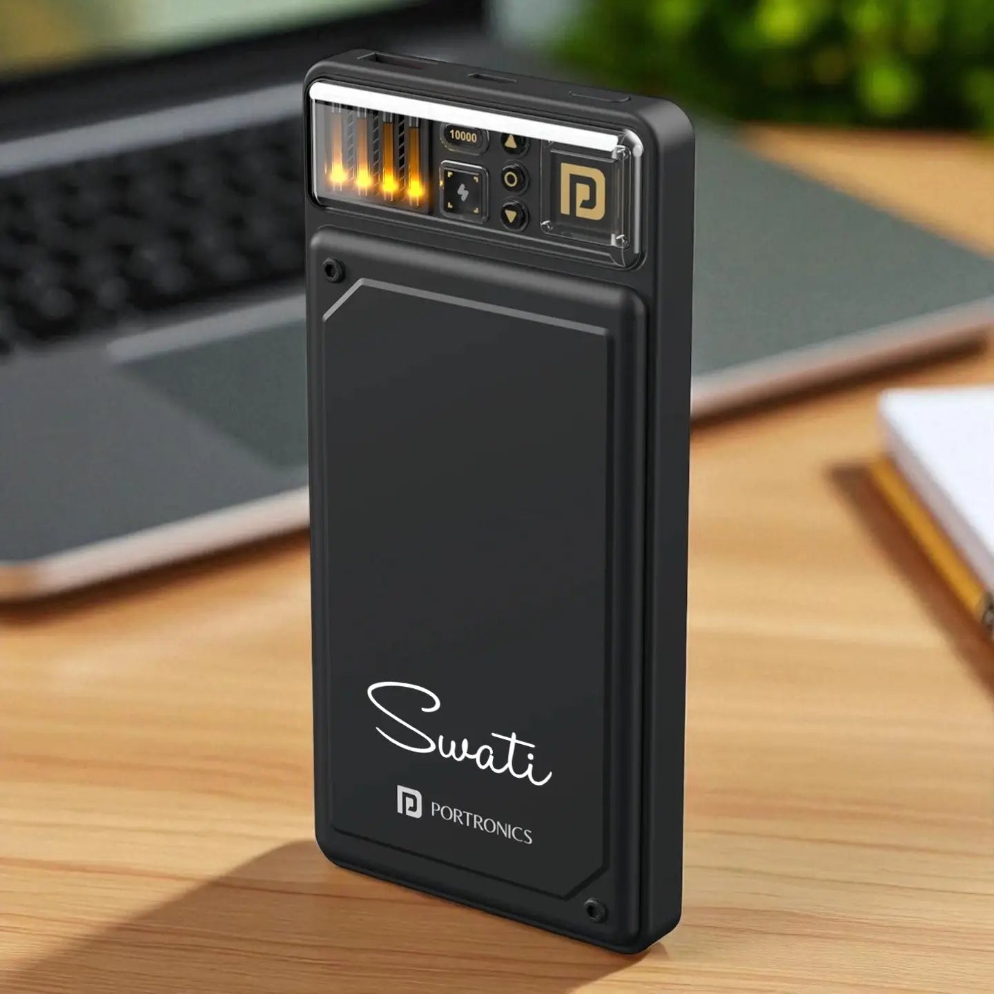 Black portable device with 'Swati' branding on a wooden surface with a laptop in the background