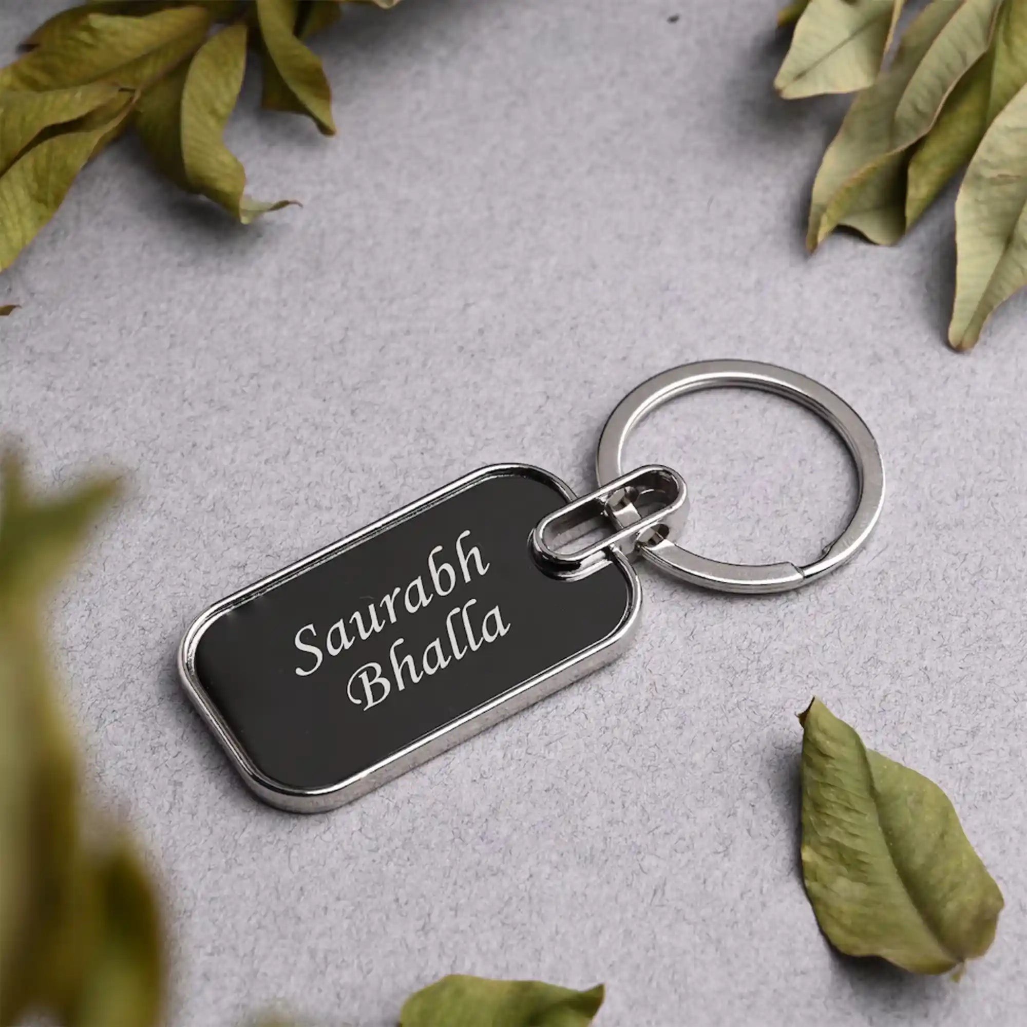 Keychain with engraved name on a gray surface with leaves