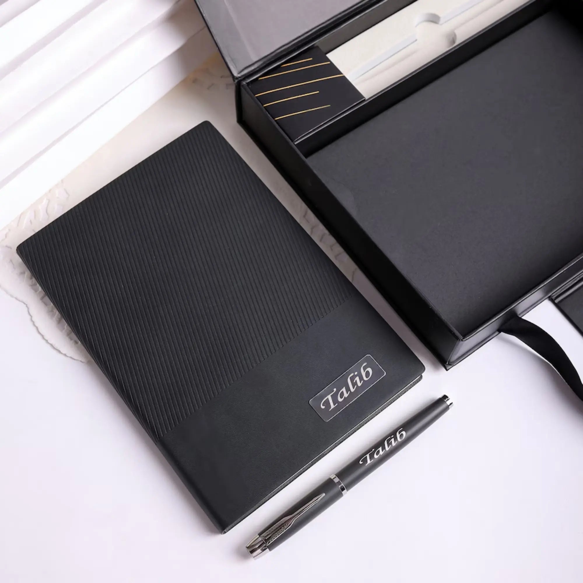 Black notebook and pen set with 'Talib' branding on a white background