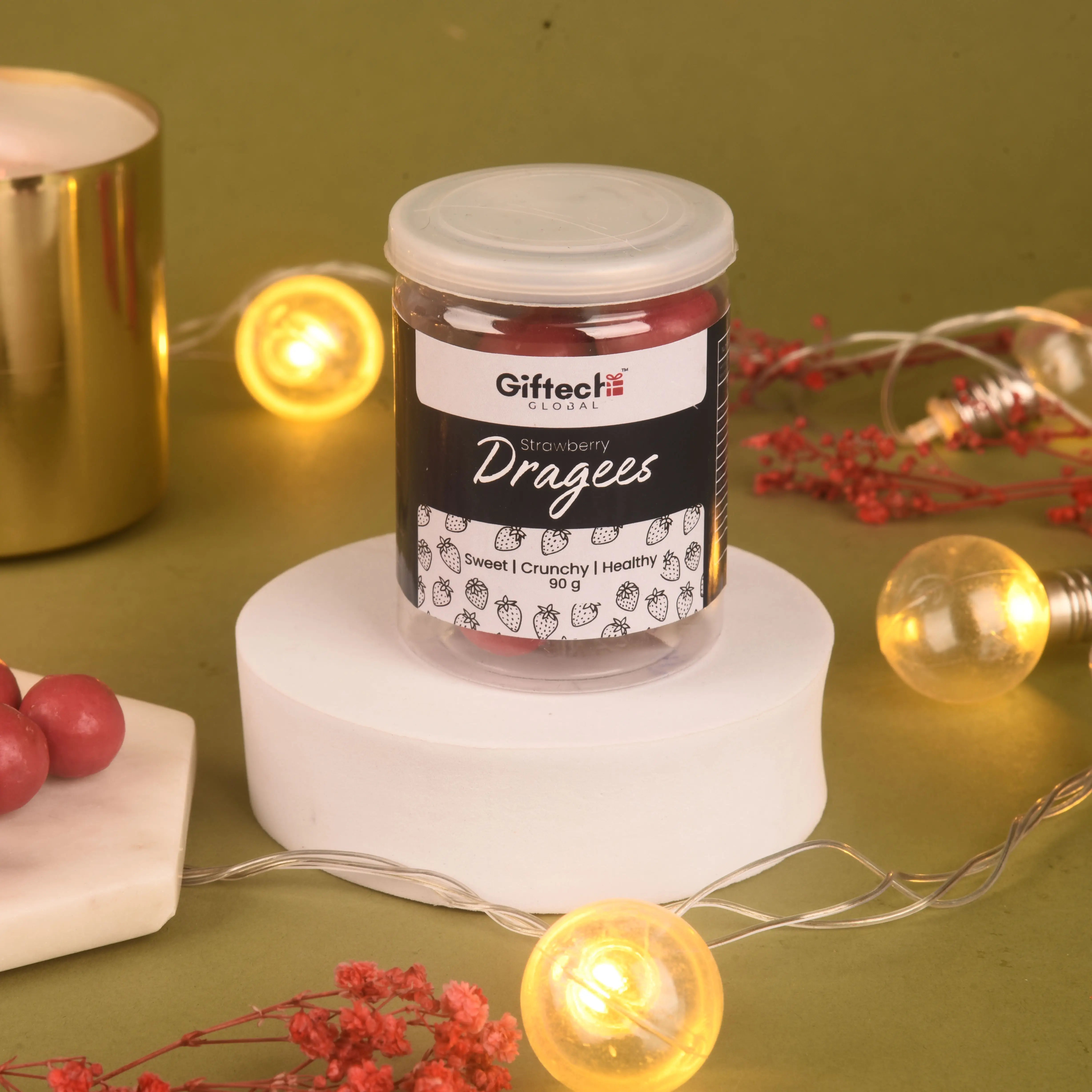 Jar of strawberry dragees on a white pedestal with decorative lights and berries on a green background
