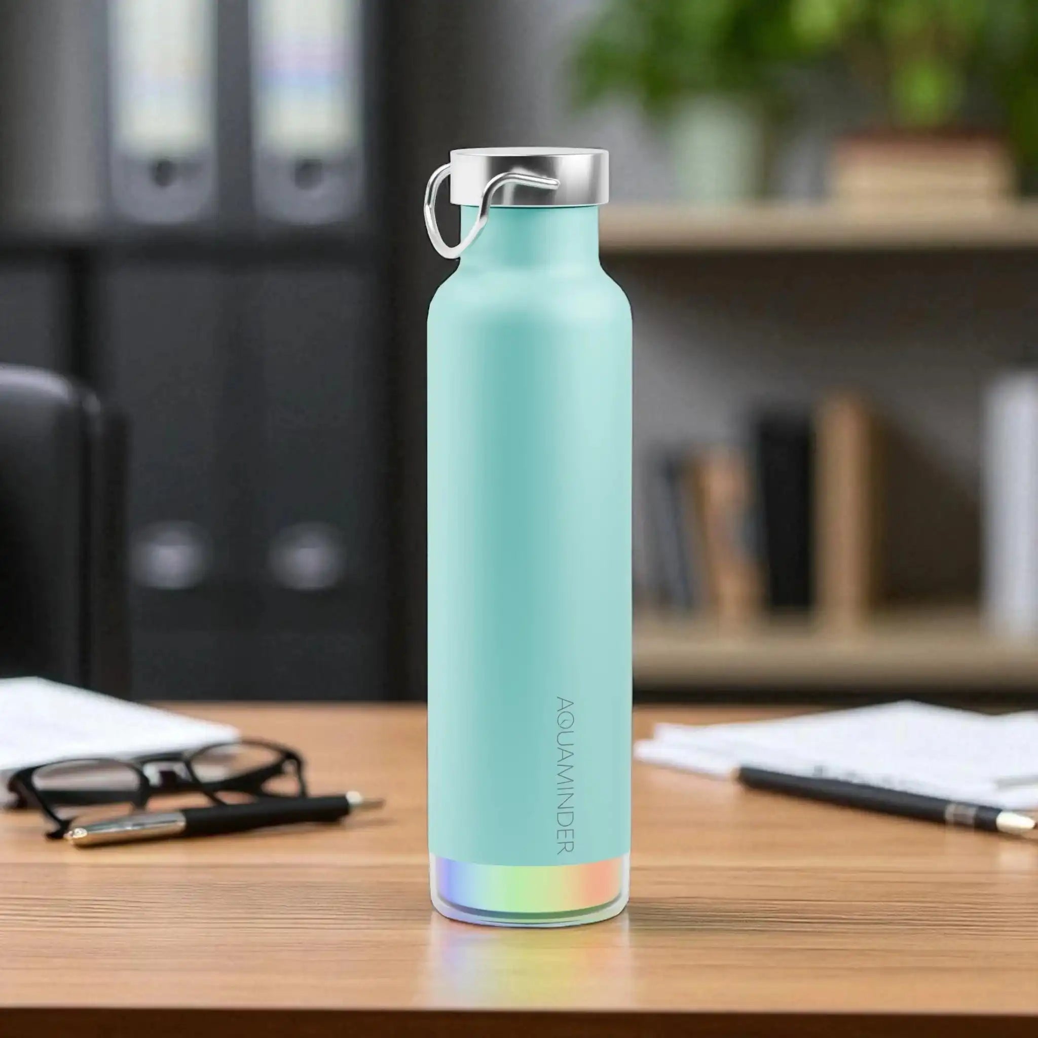 Turquoise water bottle with rainbow base on a desk