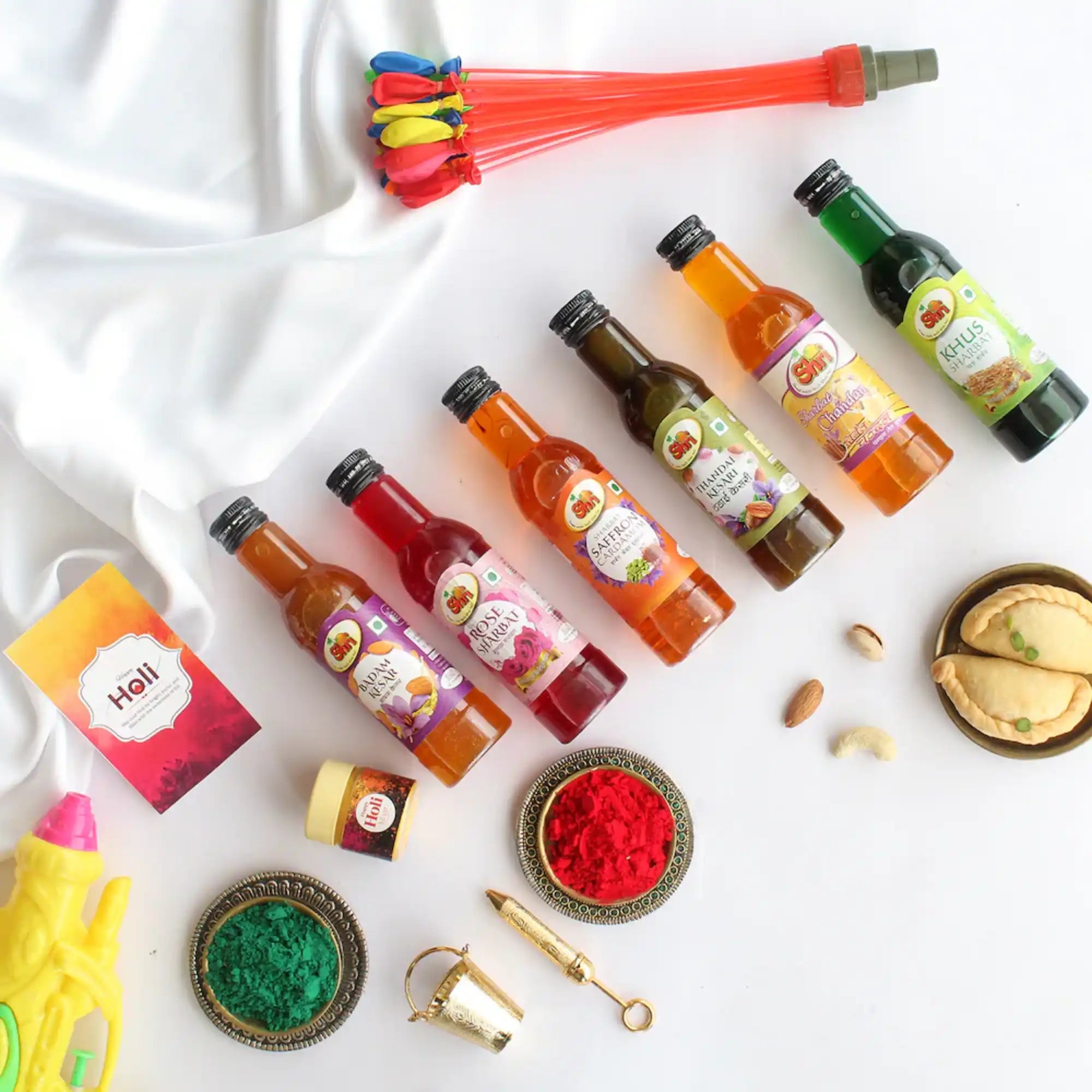 Holi party supplies with Thandai flavor bottles, colorful balloons, powders, and festive decorations