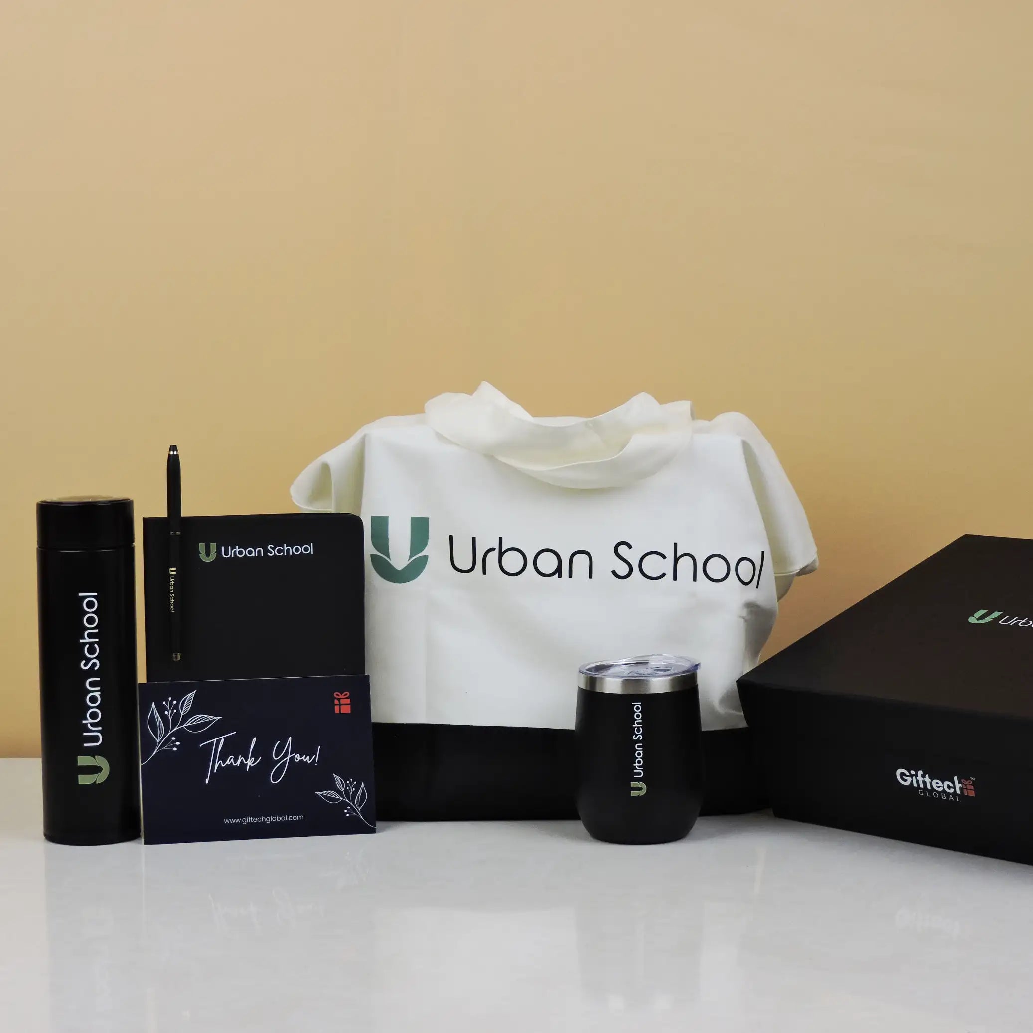 Collection of Urban School branded items including a tumbler, box, and tote bag on a beige background.