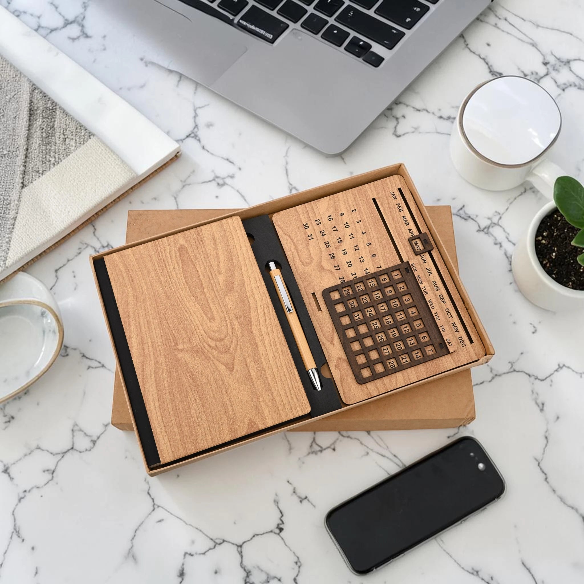 Wooden stationery set with pen, notepad, and ruler on a marble desk with laptop and phone.
