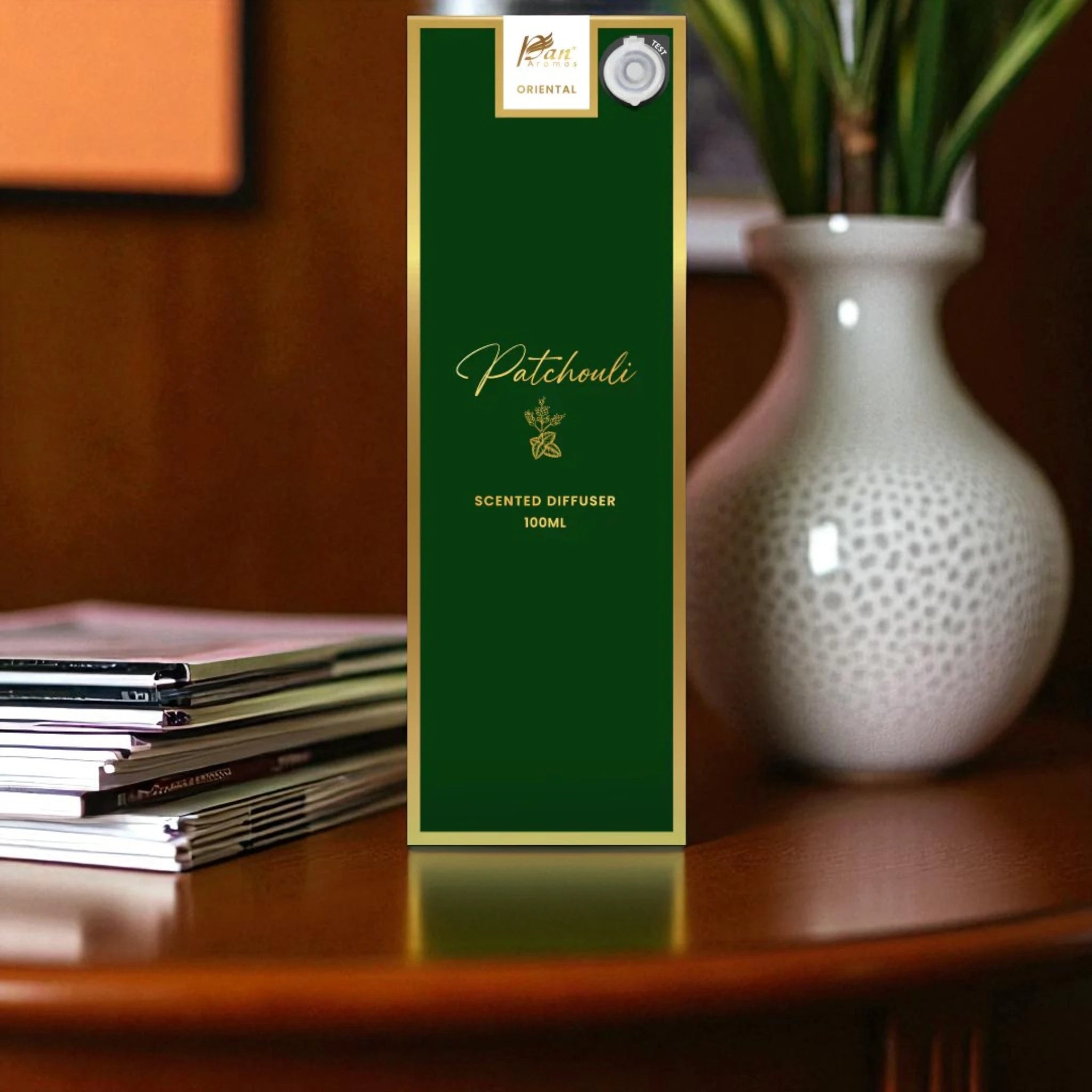 Green scented diffuser packaging on a wooden surface with a vase and books in the background