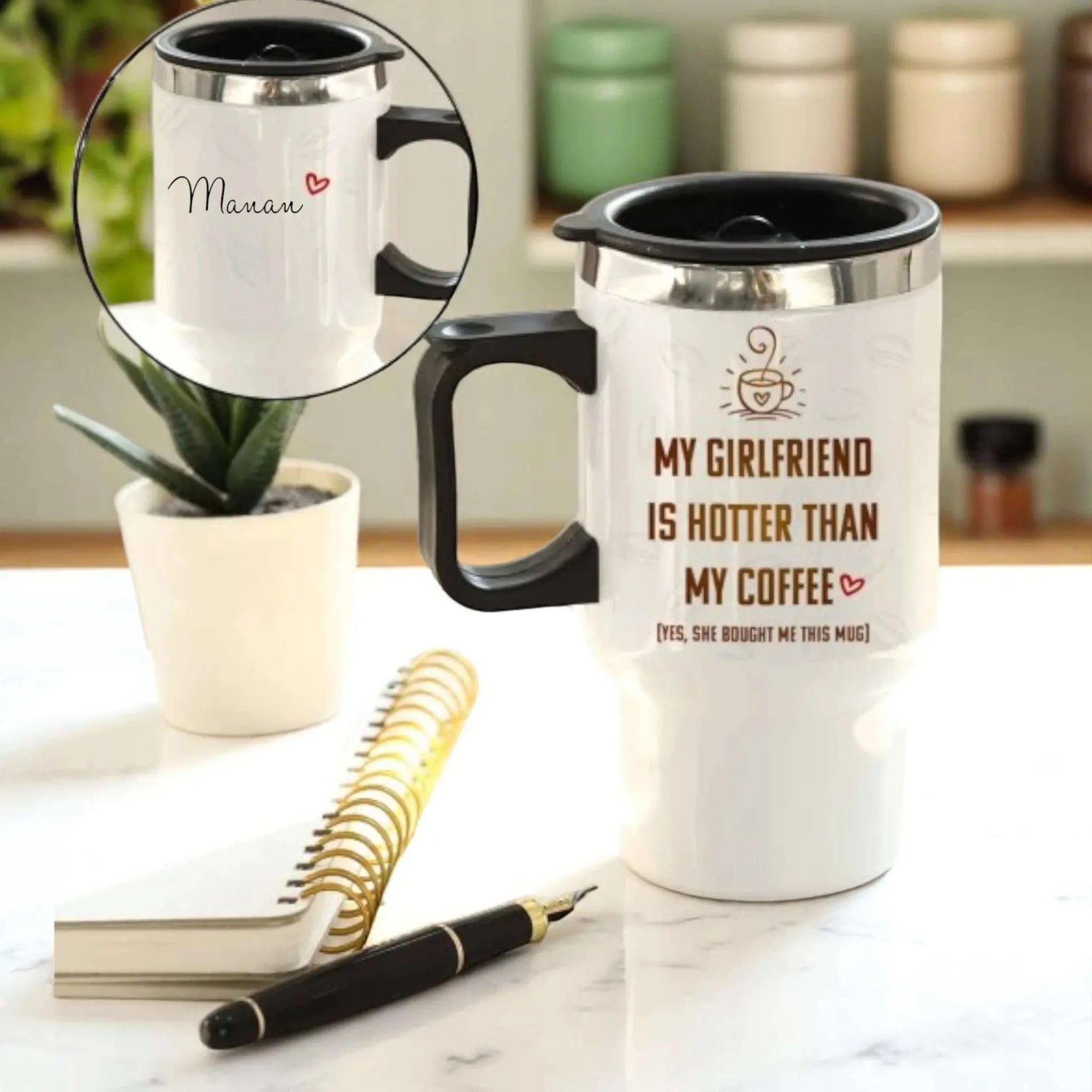 White travel mug with black handle and interior, featuring text, on a marble surface with a plant and notebook.